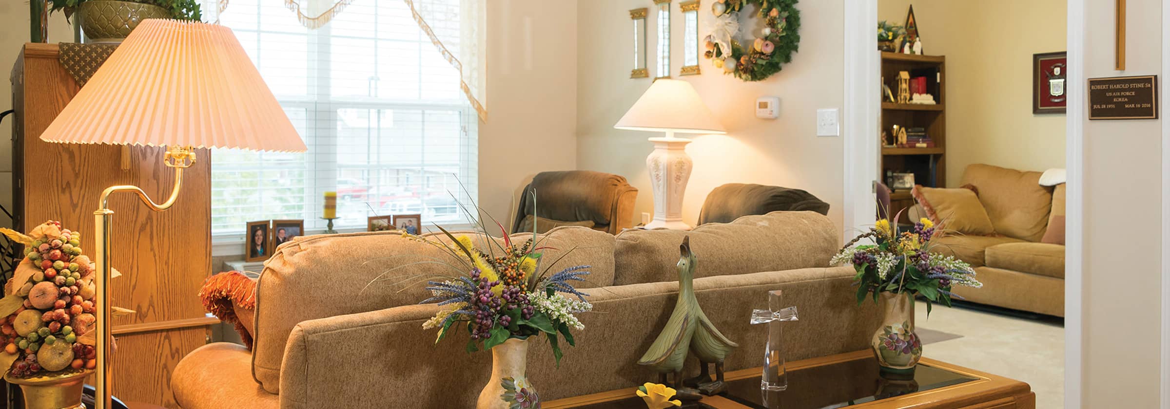 A seating area with tan couches, lamps, and flower arrangements at Traditions at Reagan Park