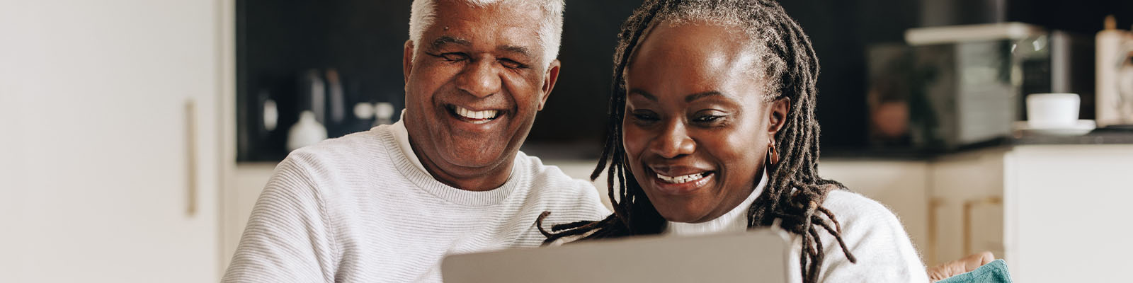 A senior man and woman sitting together on a couch looking down at a laptop