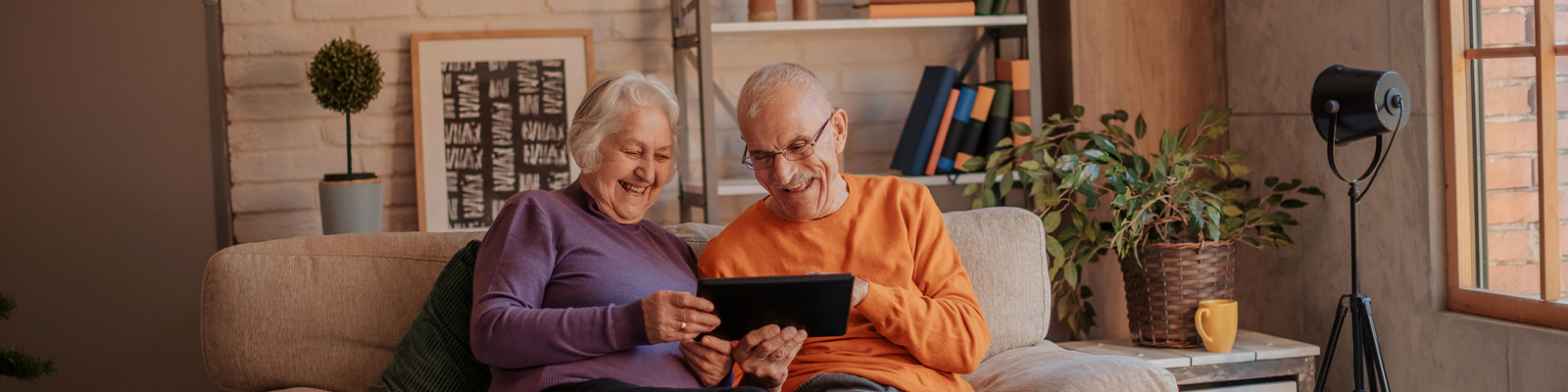 A senior man and woman sitting on a couch looking down at a smart tablet