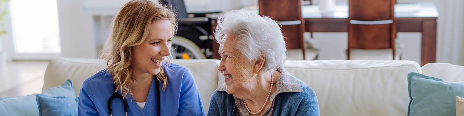 A senior woman sitting beside her nursing assistant on a white couch