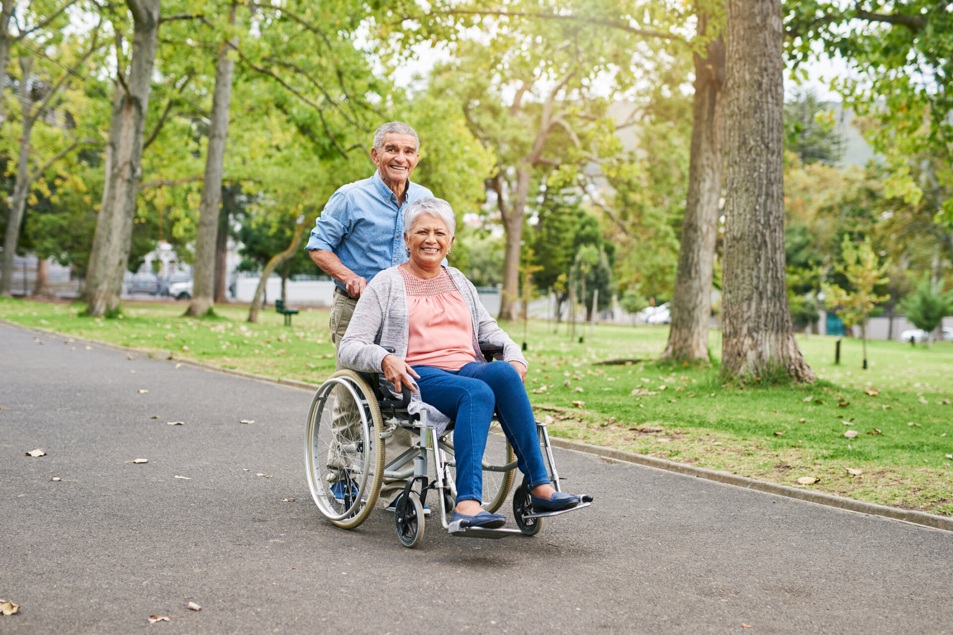 Senior man pushing his senior wife in a wheelchair outside of the Traditions at Reagan Park senior community