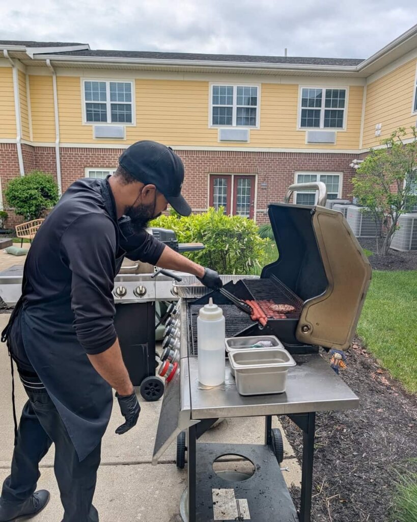 A Traditions at Reagan Park chef grills burgers and hot dogs on an outdoor grill during a Memorial Day cookout at the community.